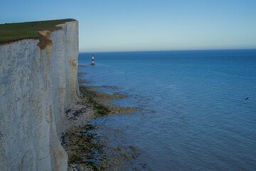 View of the red lighthouse in the bright blue water of the ocean. View of the lighthouse from the top of the cliff. Red lighthouse at the foot of the cliff.