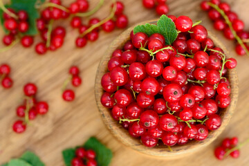 Red currant heap in a bowl. Currant red with leaf on wooden background. Organic currants with soft focus. Currant top view.
