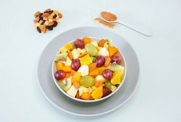 Close up on a bowl filled with a fresh and colorful fruit salad. Orange fruit, kiwi, papaya, melon, apple, almond. Brown sugar on the spoon
