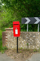 A bright red metal mailbox for sending paper letters stands along the road. An old-style mailbox.