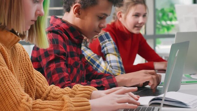 Close up of multiracial kids working on laptop at school. Diverse concentrated teen students study in computer class