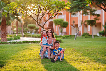 Mother with two sons on egyptian resort sitting on green grass. Family vacation.