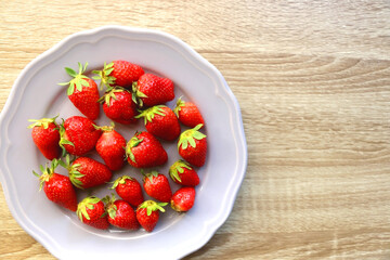 Lilac plate full of fresh strawberries on wooden table. Flat lay.