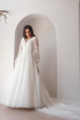 Fototapeta premium Full length bride portrait. Elegant woman in white wedding dress spinning in beige interior.