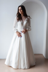 Fototapeta premium Charming young bride in luxurious wedding dress. Pretty girl in white. Emotions of happiness, laughter and smile, gray background