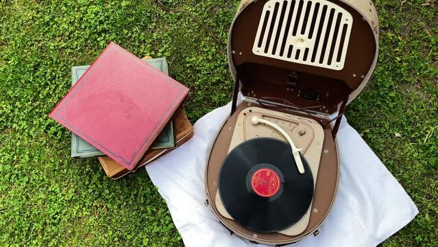 Top view of an old retro record player from the 1950s and 1960s is used outside in the garden to play music from an old vinyl record and next to it is a stack of old vinyl records