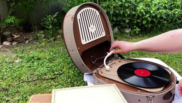 An old vinyl record is put on an old vintage turntable from the 1950s and 1960s and listening to music outside in the garden and next to it is another stack of old vinyl records