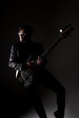 Caucasian man in glasses with bass guitar playing on a dark background