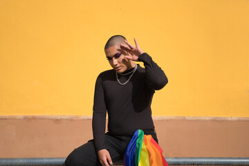 Non-binary person, young South American, heavily make up, sitting on a railing with a gay pride...
