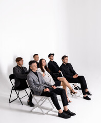 Group of six young boys and girls sitting on armchairs on a white background and thinking