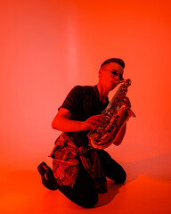 Young saxophonist in black glasses emotionally plays the saxophone sitting on the floor on his...
