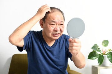 鏡を見ながら薄毛に悩む中高年の男性