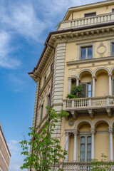 Facade of old, European building, with balconies with plants and arches. Behind a blue sky.