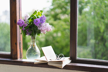 Book, glasses and lilac on a wooden window. Romantic concept. Vintage style