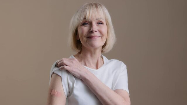 Coronavirus immunization infection covid19 vaccination happy vaccinated senior lady mature woman posing with adhesive medical plaster on arm after antivirus injection support against pandemic disease