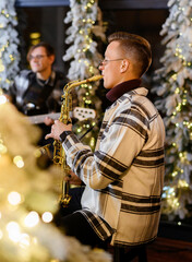 Young guy saxophonist plays the saxophone on the background of the Christmas tree