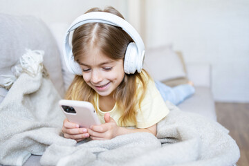 Happy small child in earphones listen to music enjoy good sound or play online game on cellphone.