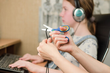 In the foreground, female hands are cutting the headphone cord with scissors, in the background is...