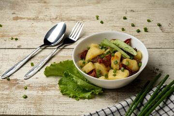 Stewed potatoes in a white cup on a white wooden table, cutlery and a checkered towel, food photo for a magazine and space for text, potatoes with meat and tomatoes, onions and lettuce