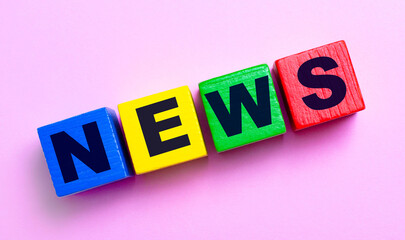 On a light pink background, multi-colored wooden cubes with the text NEWS