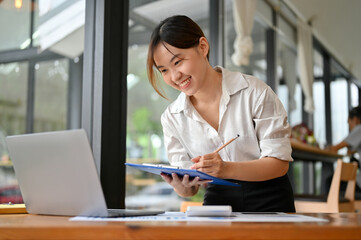 Cheerful Asian businesswoman writing something on a financial report