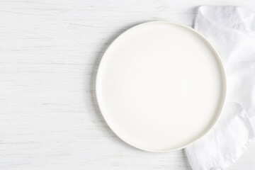 White empty plate and on linen napkin on white wooden table.