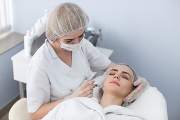 Obraz premium Woman gets injection in her face. Beauty woman giving botox injections. Young woman gets beauty facial injections in the cosmetology salon. Face aging injection. Aesthetic Medicine, Cosmetology