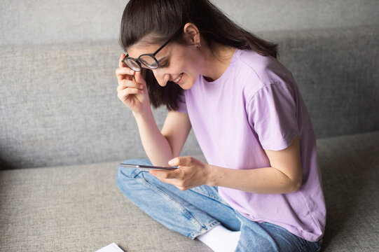 A young girl sits and looks at the phone, raised her glasses and laughs
