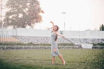 Attractive caucasian woman dancing in summer rain and enjoying water drops on green grass