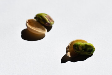 cracked green and salty pistachios near blurred nutshells on white background