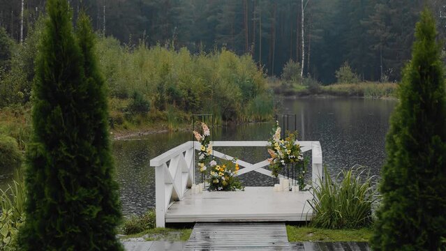 There is a wedding arch on the pond on the pier and it is raining. Cool shots in motion
