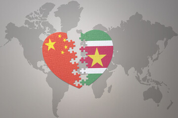 puzzle heart with the national flag of china and suriname on a world map background. Concept.
