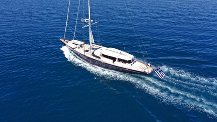 Aerial drone birds eye view photo of beautiful sailboat with blue sails cruising in the deep blue Aegean sea, Greece