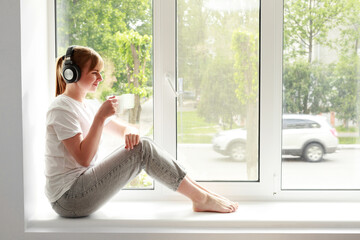 woman in headphones with a cup on the window