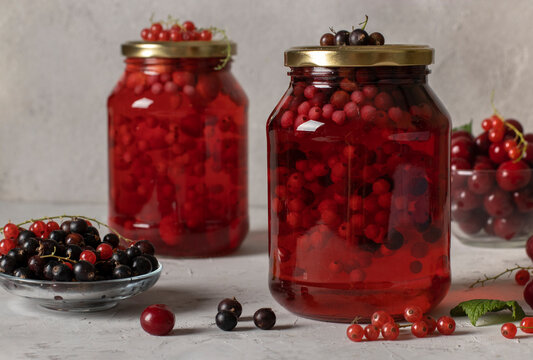 Homemade canned compote with cherries and currants in two jars on light gray background