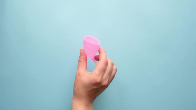 Ditching the tampon and  menstrual pad in favor of a menstrual cup. The woman's hand removes the tampon and sanitary napkin and puts the menstrual cup on the table. Footage on a blue plain background