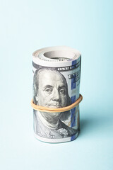 Roll of one hundred american dollars on blue background.