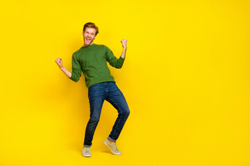 Fototapeta na wymiar Full length photo of pretty lucky man wear green pullover rising fists empty space isolated yellow color background