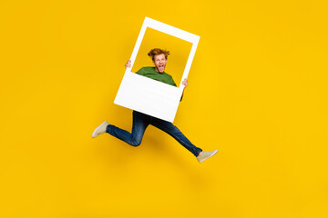 Full length photo of funny excited guy dressed sweater holding white photo frame isolated yellow...