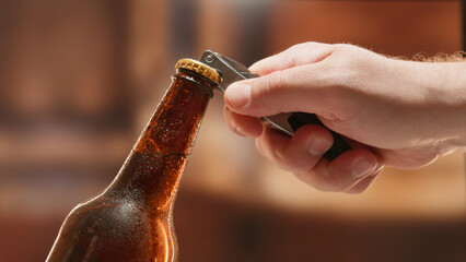Close-up man hand opens lid fresh light beer in sweating from cold dark brown glass bottle with lid...