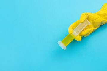 A hand in a yellow glove holds a plastic container for cleaning the toilet on a blue background. Banner with copy space. 