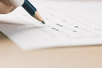 student hand testing in exercise and passing exam carbon paper computer sheet with pencil in school test room, education concept