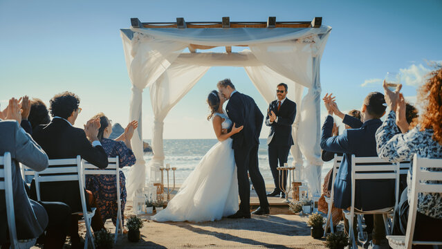 Beautiful Bride and Groom During an Outdoors Wedding Ceremony on an Ocean Beach. Perfect Venue for Romantic Couple to Get Married, Exchange Rings, Kiss and Share Celebrations with Multiethnic Friends.