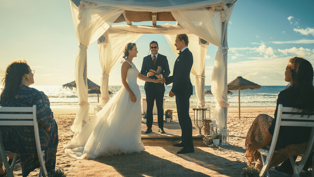 Beautiful Bride and Groom During an Outdoors Wedding Ceremony on an Ocean Beach at Sunset. Perfect Venue for a Couple to Marry, Exchange Rings, Kiss and Share Celebrations with Multiethnic Friends.
