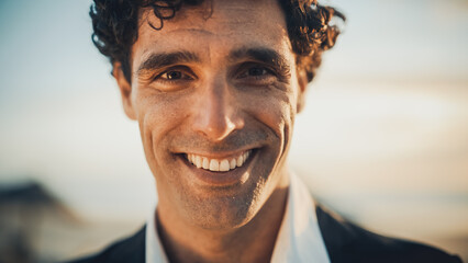 Close Up Portrait of a Happy Young Adult Male with Curly Hair and Brown Eyes Posing for Camera. Handsome Multiethnic Caucasian Male in a Suit Charmingly Smiling. Warm Color Edit. - obrazy, fototapety, plakaty