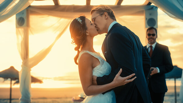 Beautiful Bride and Groom During an Outdoors Wedding Ceremony on an Ocean Beach at Sunset. Perfect Venue for a Couple to Marry, Exchange Rings, Kiss and Share Celebrations with Multiethnic Friends.