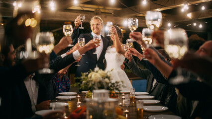 Beautiful Bride and Groom Celebrate Wedding at an Evening Reception Party. Newlyweds Propose a Toast to Happy Marriage, Standing at a Dinner Table with Best Multiethnic Diverse Friends.