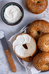 bagel cut in half and spread with cream cheese, placed inside basket full of sesame bagels on white...