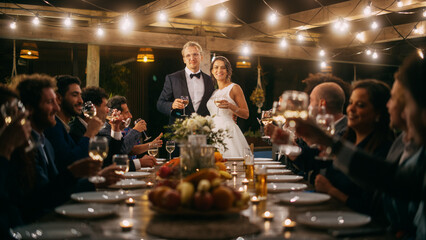 Beautiful Bride and Groom Celebrate Wedding at an Evening Reception Party. Newlyweds Propose a Toast to Happy Marriage, Standing at a Dinner Table with Best Multiethnic Diverse Friends.