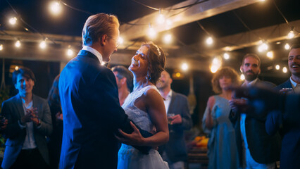 Beautiful Bride in White Dress and Groom in Stylish Black Suit Celebrate Wedding at an Evening Reception Party. Newlyweds Dancing at a Venue with Best Multiethnic Diverse Friends.